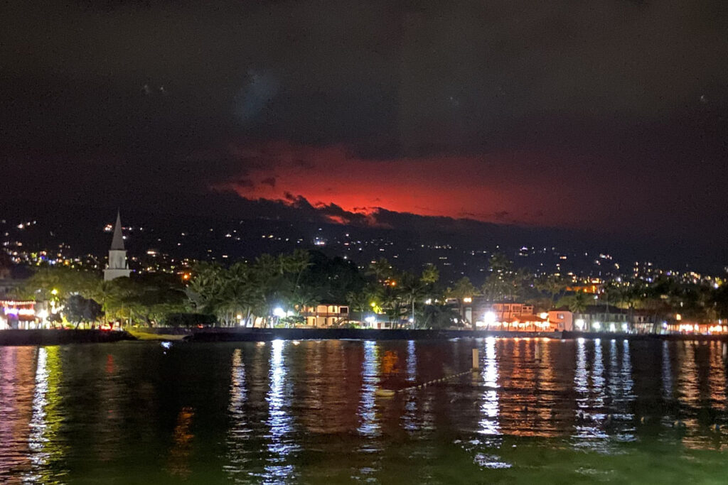 Night shot of a bay with a glowing volcano in the background
