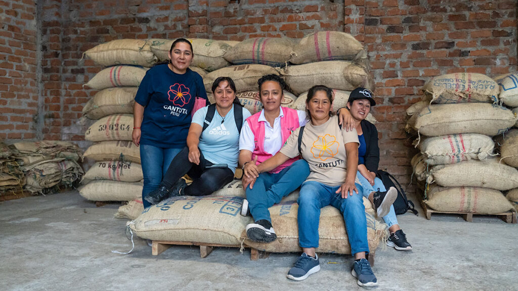 5 women sitting on bags of coffee at a small coffee factory in Colombia

